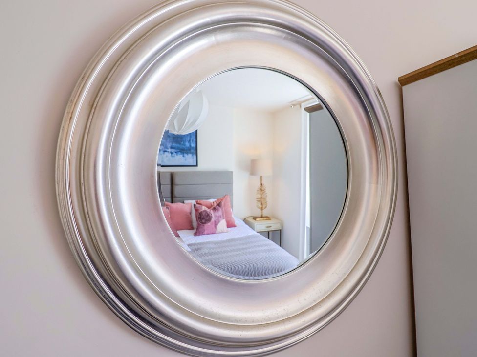 A mirror reflecting a bed with pillows and a lamp at Pebble Cove in Lyme Regis