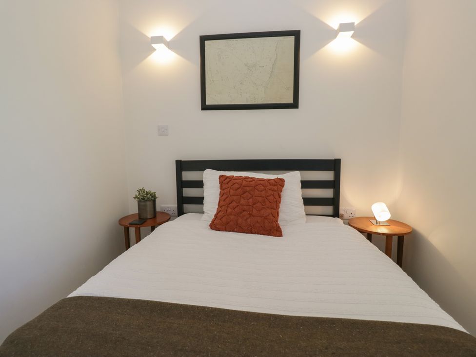 A bedroom with a bed, two bedside tables, and wall art at Driftwood Cottage in Ulverston