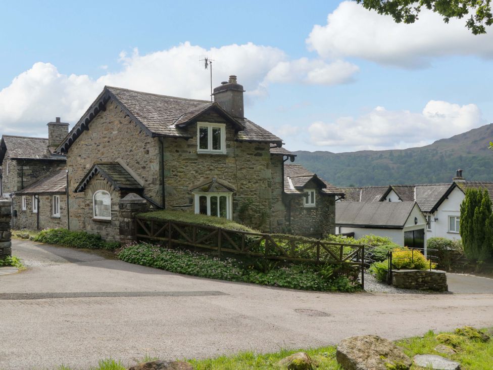 A stone cottage with a fence and driveway at Hollens Cottage in Grasmere