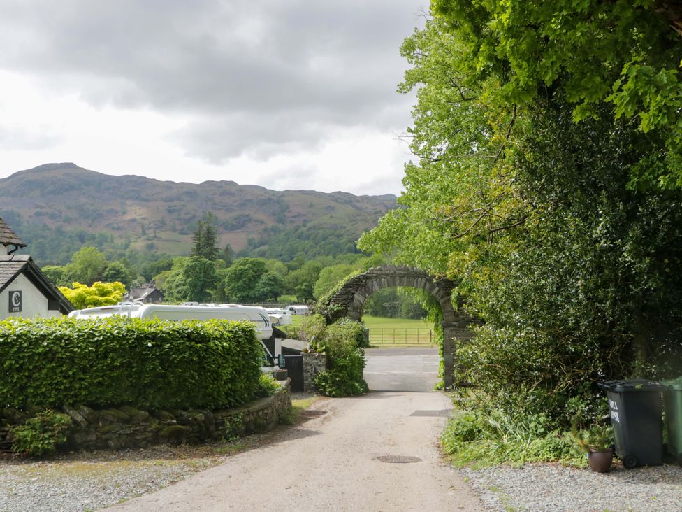 A driveway leading through an archway with trees and mountains at Hollens Cottage in Grasmere