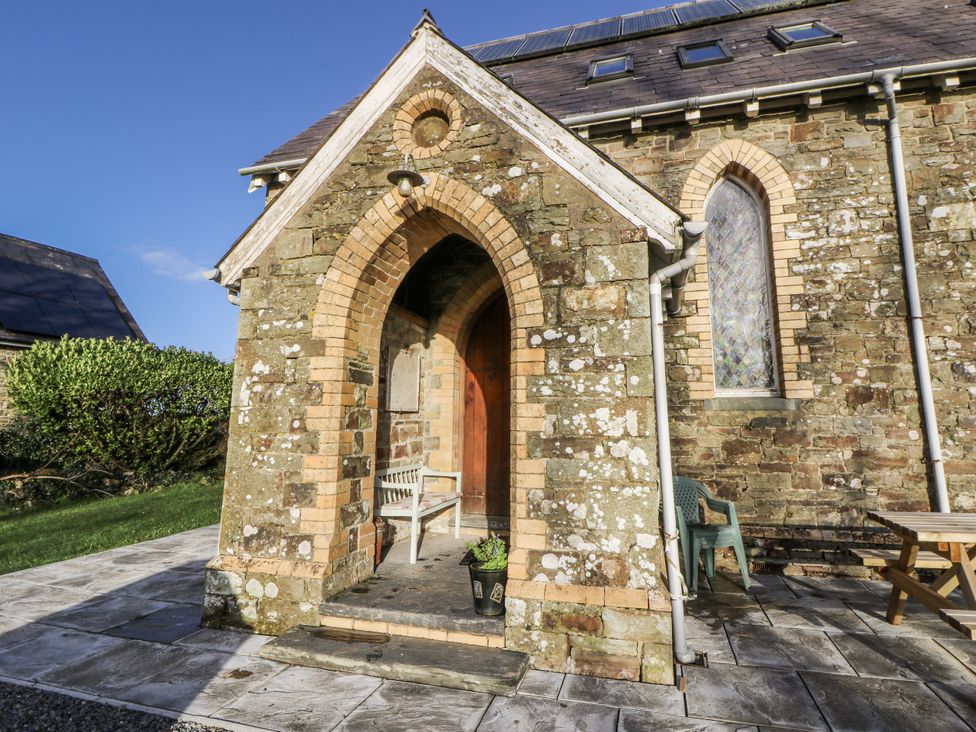 An exterior entrance with an arched doorway and chair at Church Llygad Y Dyffryn Sarnau near Brynhoffnant