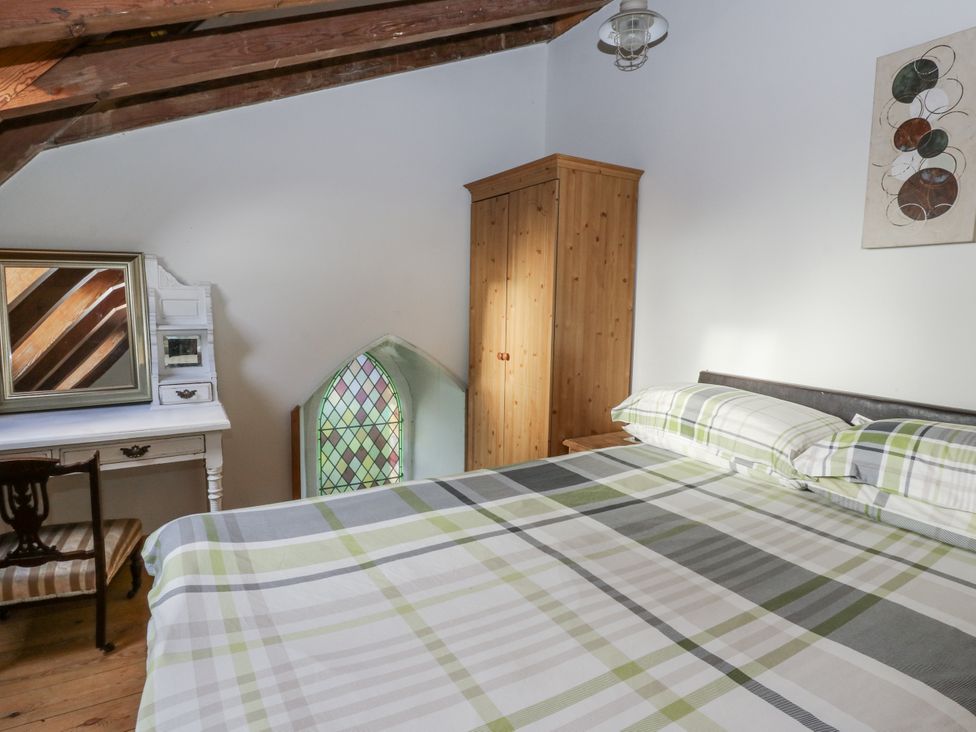 A bedroom with a bed, wardrobe, mirror and a stained glass window at Church Llygad Y Dyffryn Sarnau near Brynhoffnant
