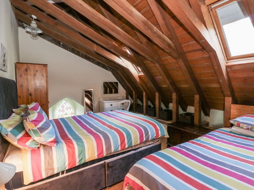 A bedroom with two beds, a nightstand, and a window at Church Llygad Y Dyffryn in Sarnau near Brynhoffnant