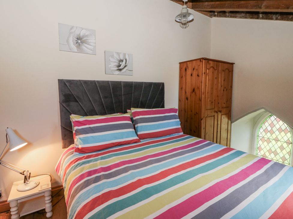 A bedroom with a striped bed cover and wooden wardrobe at Church Llygad Y Dyffryn in Sarnau near Brynhoffnant