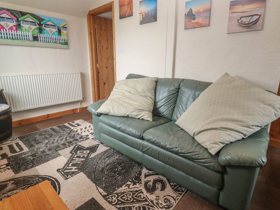 A living room with a sofa and wall art at Horseshoe Cottage Near Holywell Bay