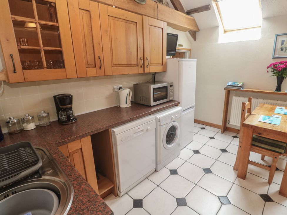A kitchen with appliances and a dining table at Horseshoe Cottage near Holywell Bay