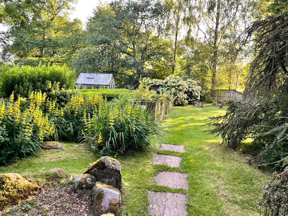 A garden with a greenhouse and pathway at Pittencleroch Mill in Crieff