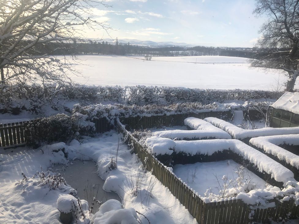 A snowy garden with a fence and field at Pittencleroch Mill in Crieff