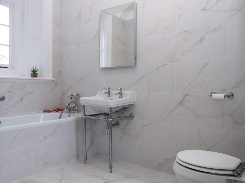 A bathroom with a bathtub, sink, toilet, and mirror at Alston Hall Battisborough Cross