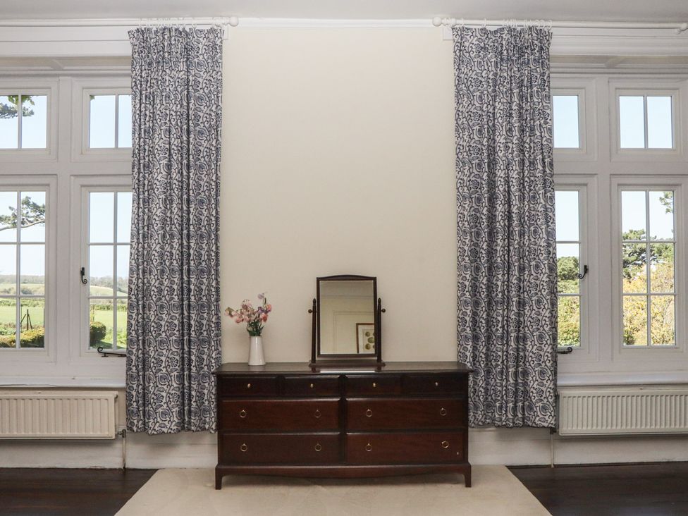 A dresser with a mirror and flower vase near windows at Alston Hall near Mothecombe Beach