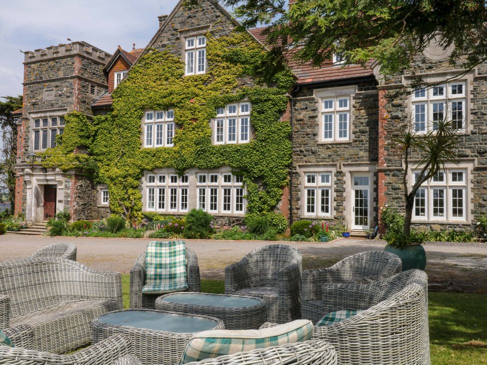 An outdoor view of a house covered in ivy and garden furniture at Alston Hall near Mothecombe Beach