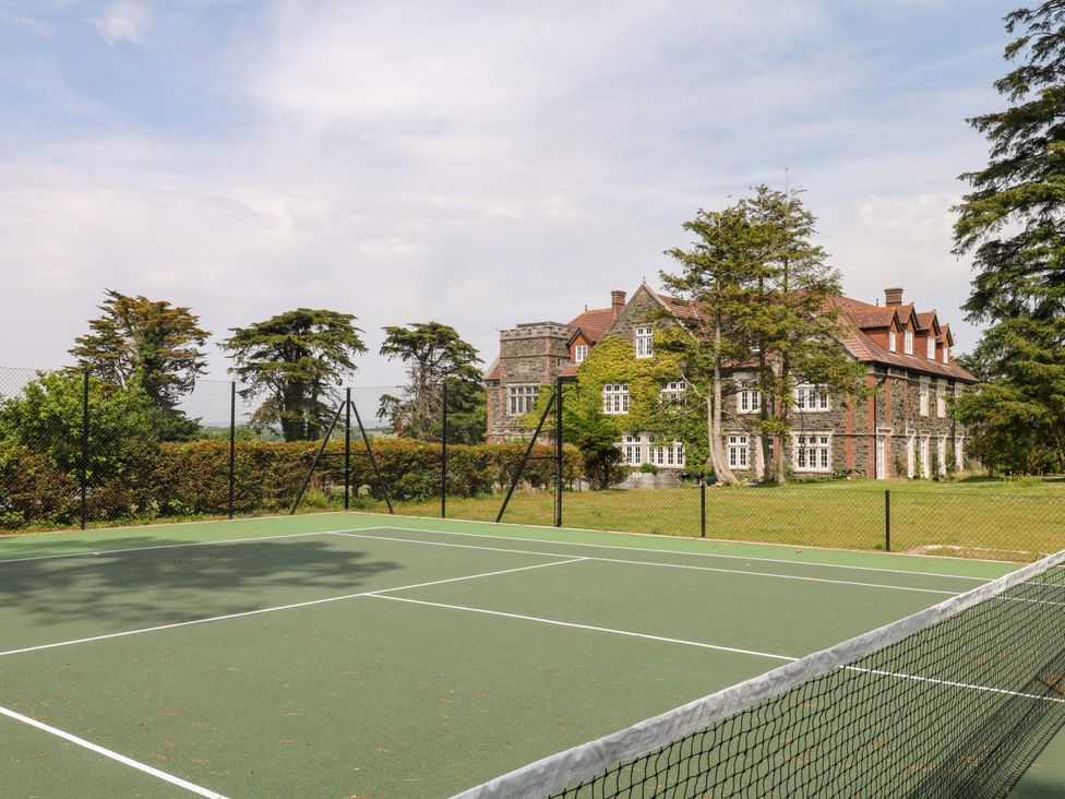 A tennis court in front of a large house surrounded by trees at Alston Hall near Mothecombe Beach