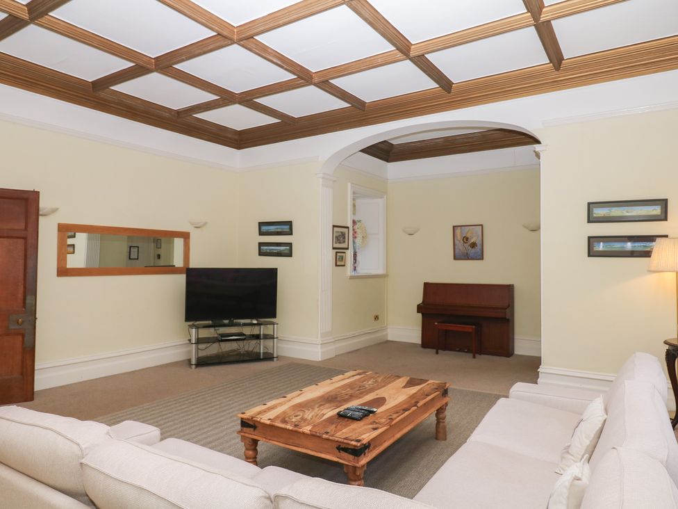 A living room with a sofa, coffee table, television, and piano at Alston Hall near Mothecombe Beach