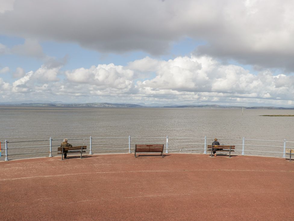 A view of two people sitting on benches by the water at Cockle Bay Cottage in Heysham