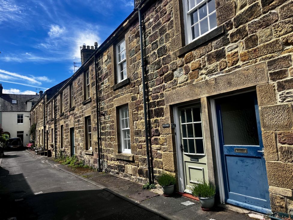 A stone row house with multiple front doors and windows on a narrow street at Aln Cottage in Alnmouth