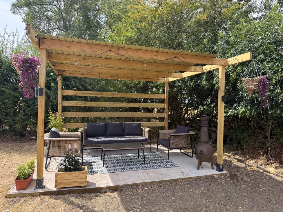 An outdoor seating area with a sofa and chairs under a pergola at Little Acre Church Lench near Harvington