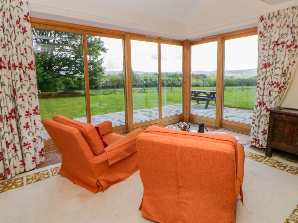 A sunroom with orange sofas and a view of the garden at Bryn Isaf in Swyddffynnon near Pontrhydfendigaid