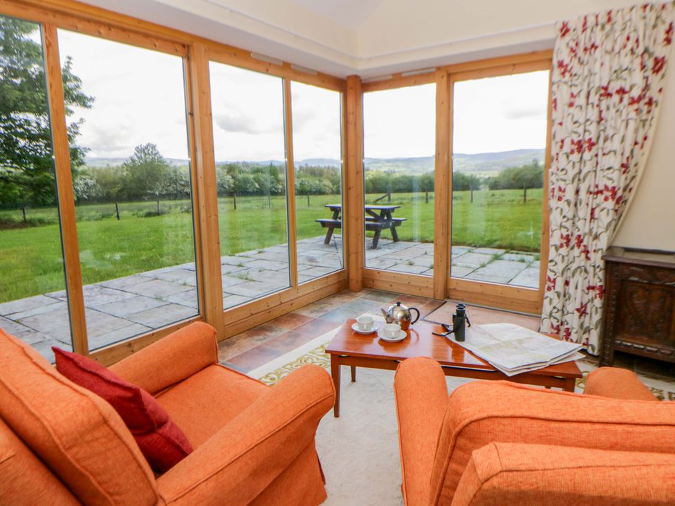 A conservatory with orange armchairs and a table with a tea set at Bryn Isaf near Swyddffynnon