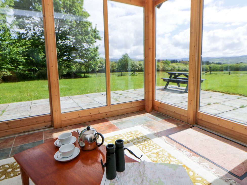 A conservatory with a table set for tea and a view of the garden at Bryn Isaf in Swyddffynnon near Pontrhydfendigaid