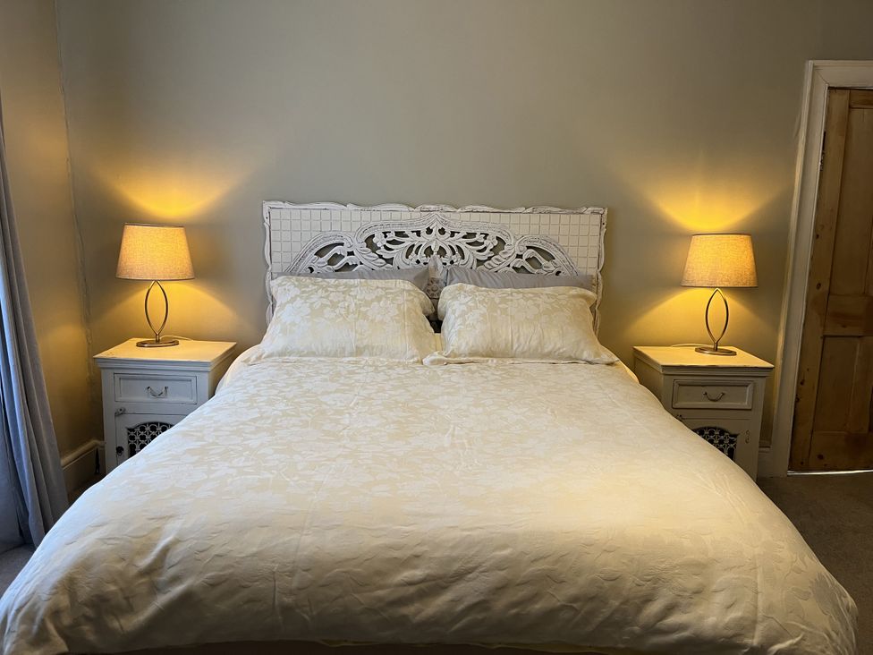 A bedroom with a bed with a carved white headboard two bedside tables with lamps and a wooden door at Humphreston House in Temple Cloud