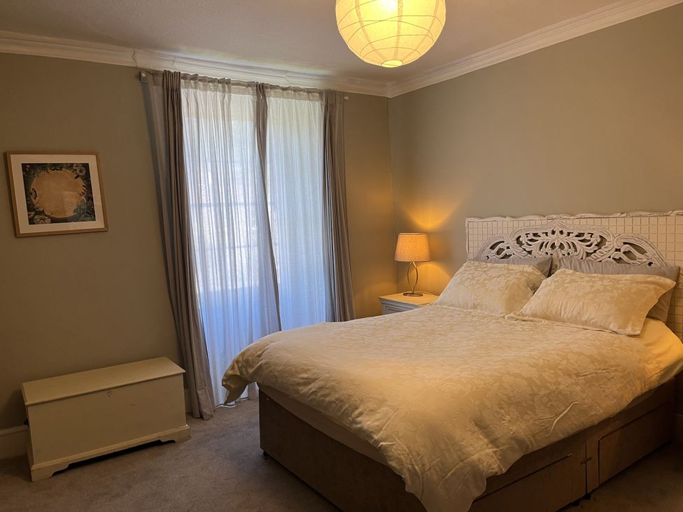 A bedroom with a bed two pillows a nightstand lamp a chest a framed picture and a window with curtains at Humphreston House Temple Cloud