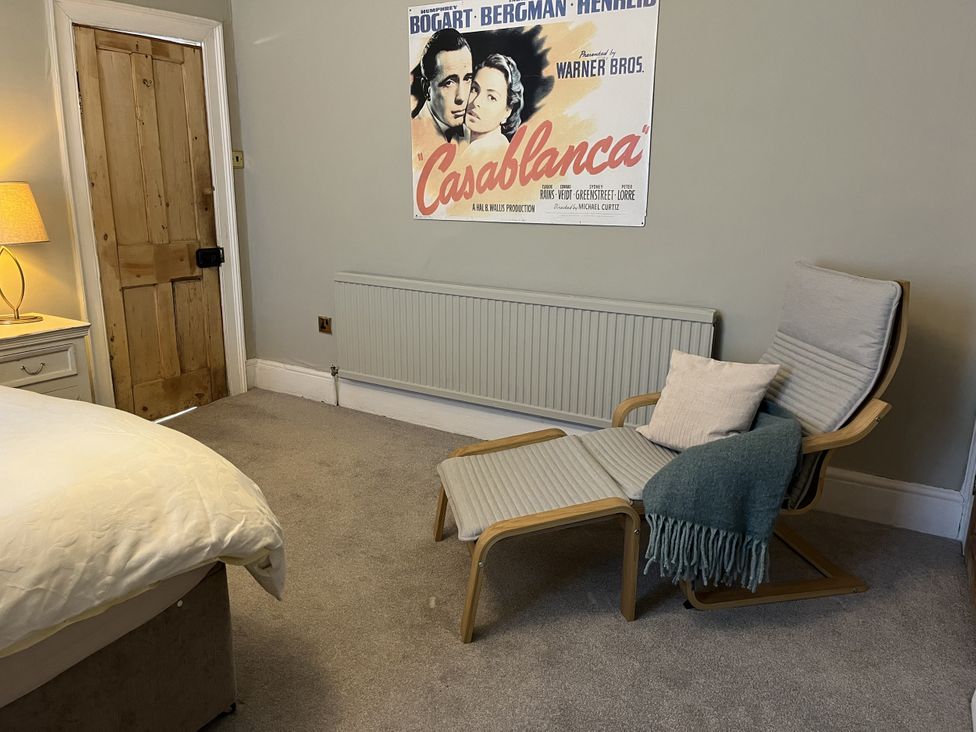 A bedroom with a bed a wooden door a dresser with a lamp a lounge chair with a pillow and blanket and a Casablanca movie poster on the wall at Humphreston House in Temple Cloud