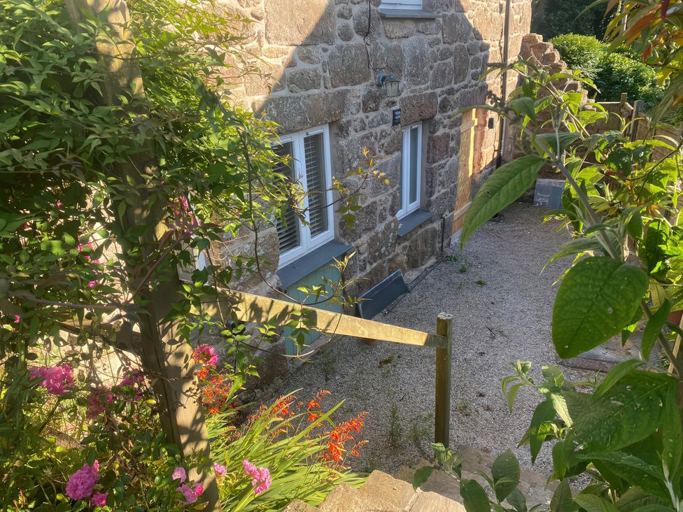 An outdoor view of a stone house with flowers and gravel at Mys Hedra Farm in Penzance