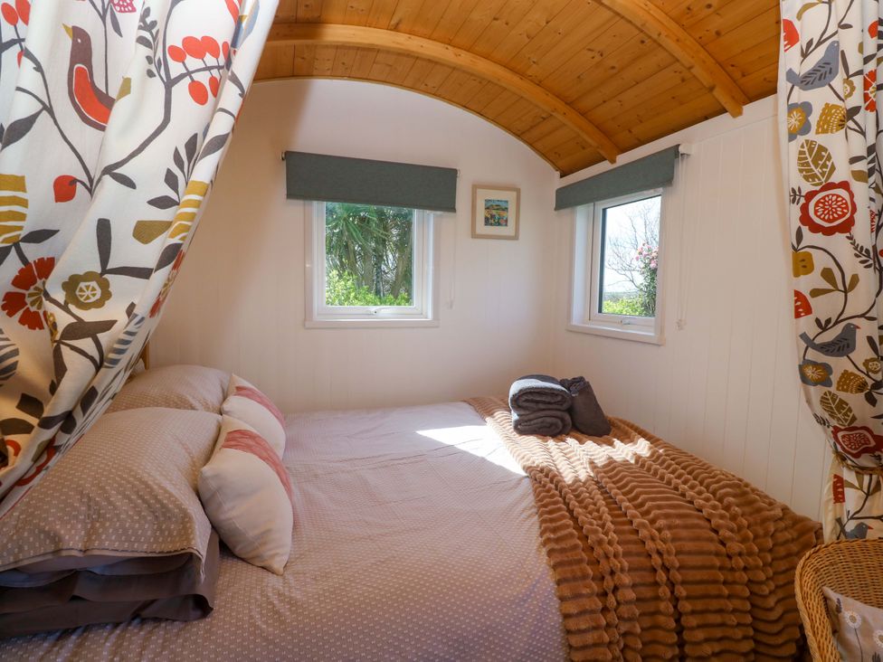 A bedroom with a bed and windows at Higher Merther Farm Shepherds Hut in Helston