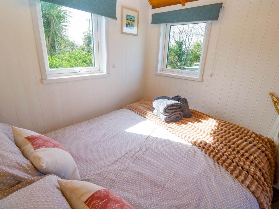 A bedroom with a double bed and windows at Higher Merther Farm Shepherds Hut Helston