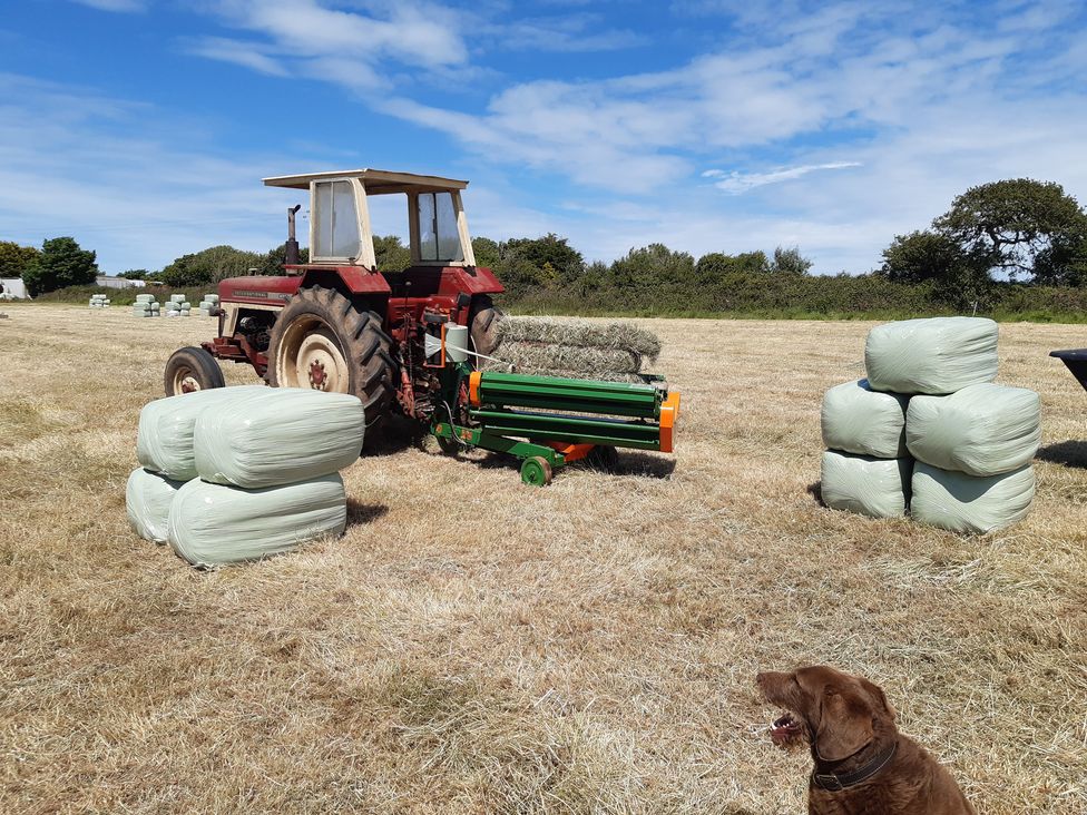 A tractor and baler in a field with hay bales at Higher Merther Farm Shepherds Hut Sithney near Helston