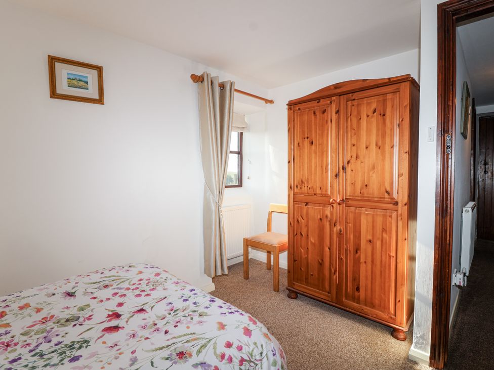 A bedroom with a bed, wardrobe, and chair at The Hayloft in Common Moor near Liskeard