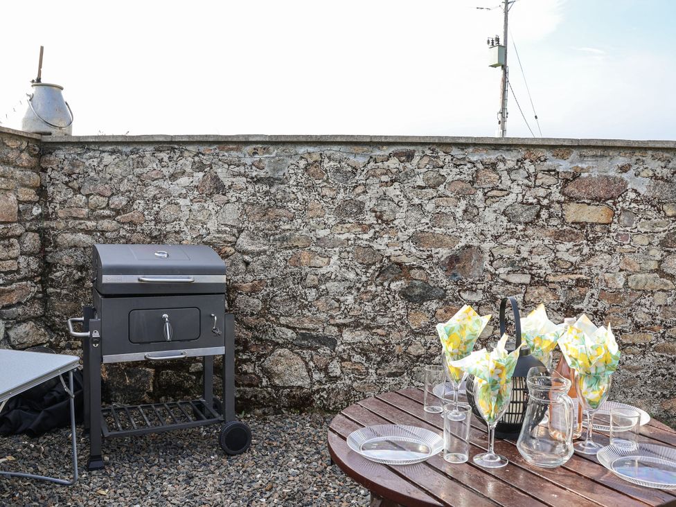 An outdoor area with a grill and a table set with plates and glasses at The Byre in Common Moor near Liskeard
