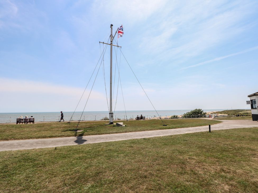 An outdoor area with a flagpole and a bench near the sea at Iona Cottage Southwold