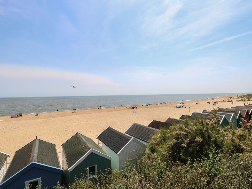 A beach with colorful beach huts and people on the sand at Iona Cottage Southwold
