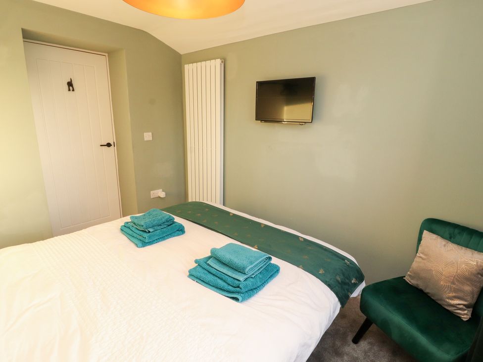 A bedroom with a bed, towels on top, television, radiator, and a chair at 10 Keekle Terrace in Keekle near Cleator Moor