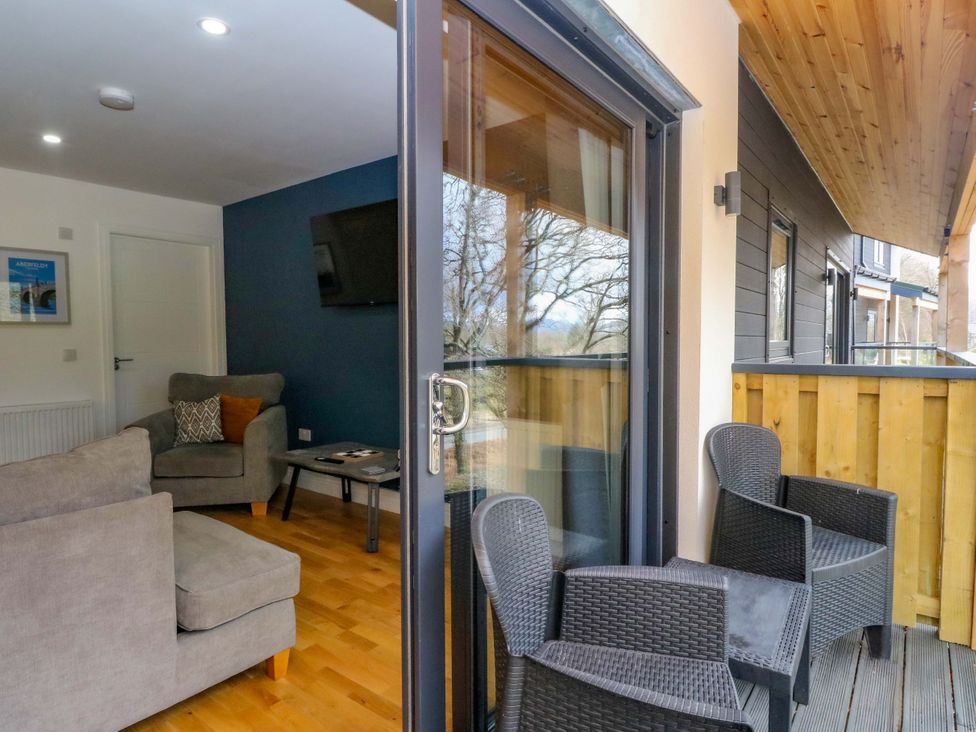 A living room with a sofa and armchair leading to a balcony at 25 Strathtay Lodges in Aberfeldy