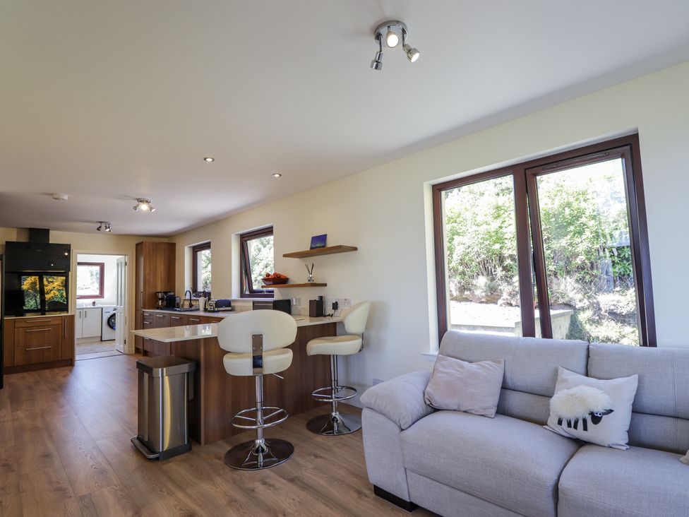 An open kitchen and living area with bar stools and a sofa near windows at Calmdale in Inverasdale near Poolewe