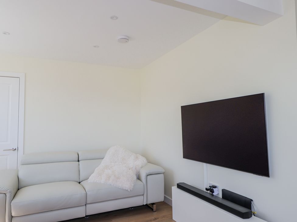 A room with a white leather sofa and a wall mounted television at Calmdale in Inverasdale near Poolewe