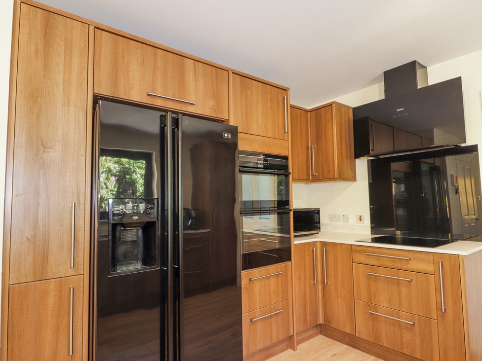 A kitchen with wooden cabinets a black refrigerator built in oven microwave and black stovetop at Calmdale Inverasdale near Poolewe