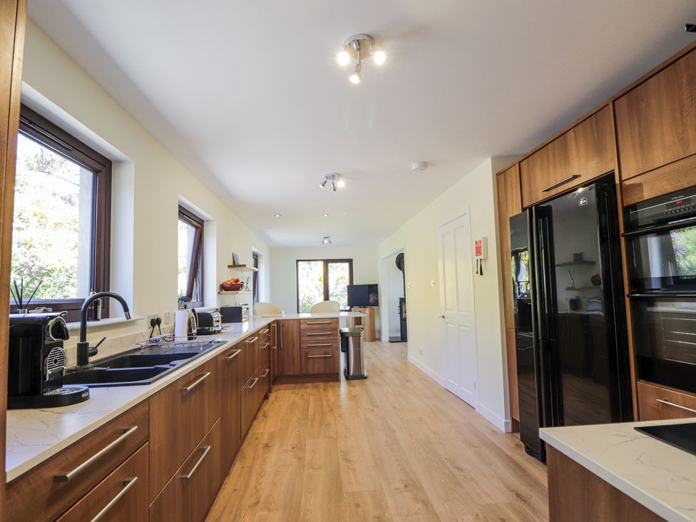A kitchen with wooden cabinets black appliances and windows along one wall at Calmdale in Inverasdale near Poolewe