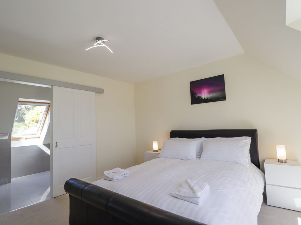 A bedroom with a double bed towels on the bed bedside tables lamps and a door to a bathroom at Calmdale in Inverasdale near Poolewe