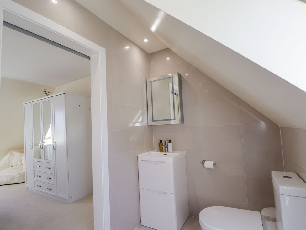 A bathroom with toilet and small sink cabinet connected to a bedroom with white wardrobe at Calmdale Inverasdale near Poolewe