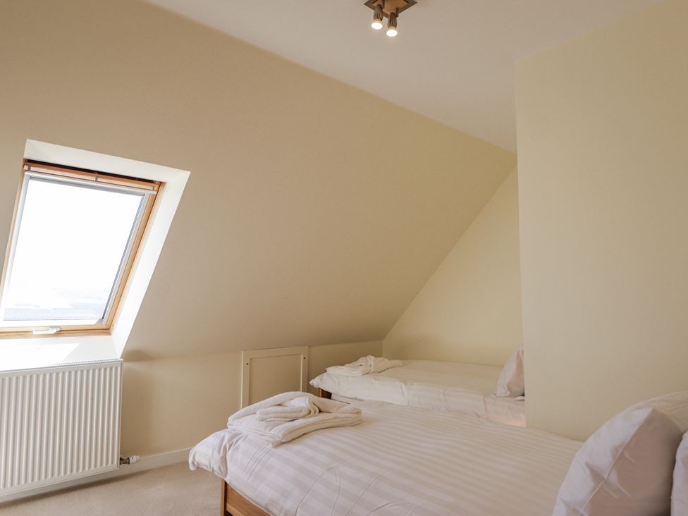 A bedroom with two single beds white linens and a slanted ceiling with a skylight window at Calmdale in Inverasdale near Poolewe