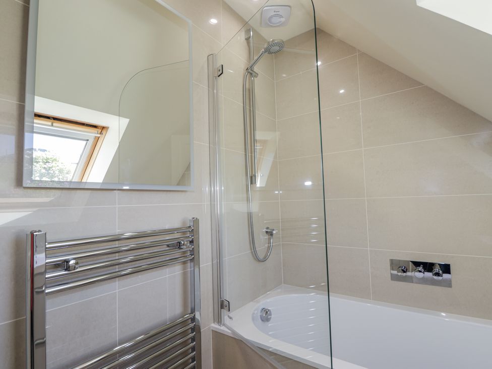 A bathroom with a bathtub shower combination a wall-mounted mirror a heated towel rail and a window at Calmdale in Inverasdale near Poolewe
