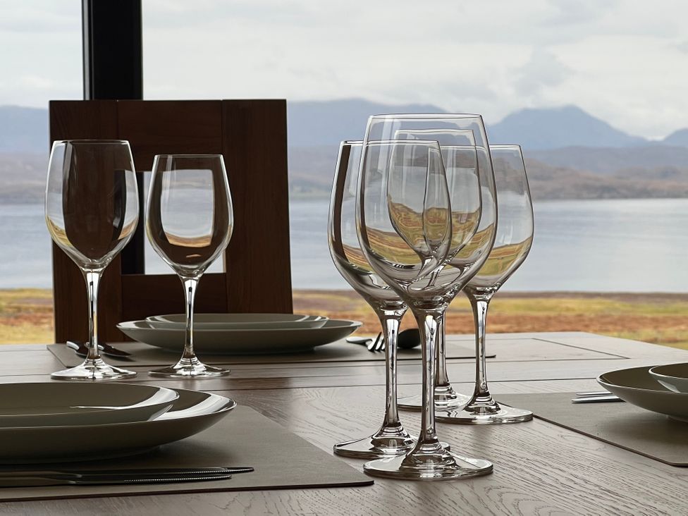 A dining table set with wine glasses plates and cutlery with a view of water and mountains at Calmdale in Inverasdale near Poolewe