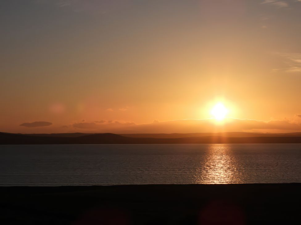 A sunset over a body of water with hills in the background at Calmdale Inverasdale near Poolewe