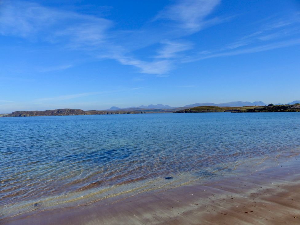 A coastal scene with a sandy beach and clear water under a blue sky with distant hills at Calmdale in Inverasdale near Poolewe