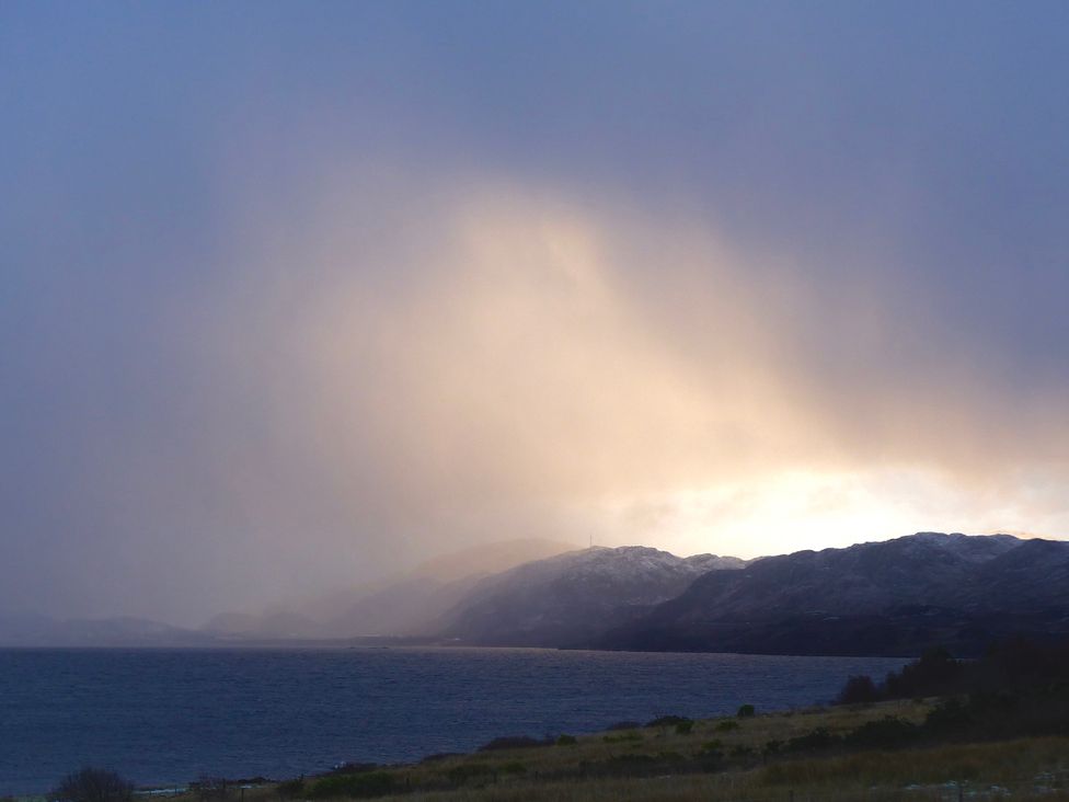 A coastal landscape with water in the foreground and mountains in the background at Calmdale Inverasdale near Poolewe