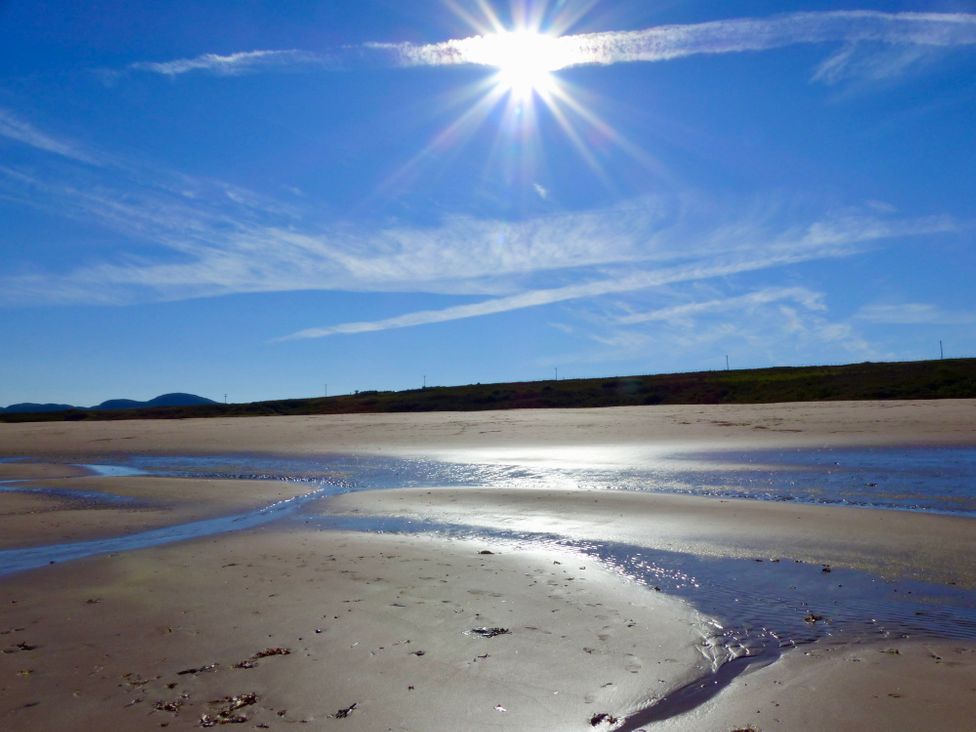 A sandy beach with shallow water streams under a bright sun and blue sky at Calmdale in Inverasdale near Poolewe
