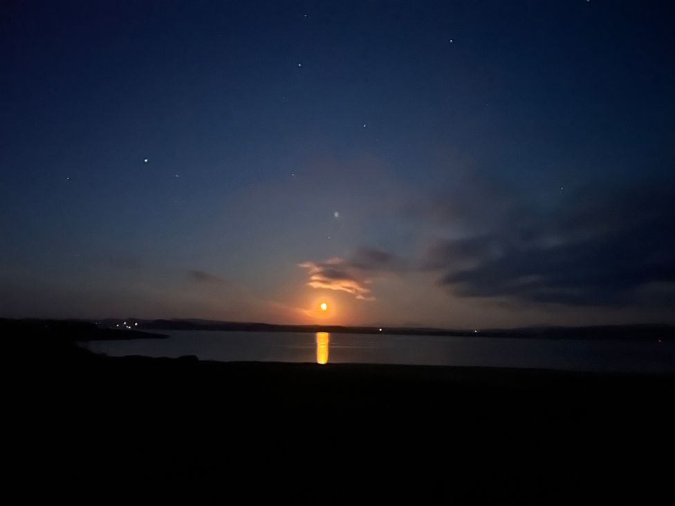 A night sky with a glowing moon and stars over a body of water at Calmdale in Inverasdale near Poolewe